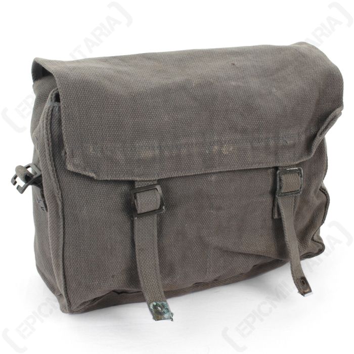 Front view of a grey canvas satchel bag with a top flap closure, secured shut with two canvas straps. The bag is turned slightly to the left, and is on a white background