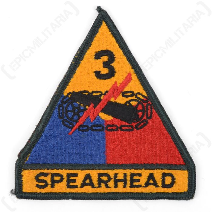 Front view of triangular embroidered patch with 'SPEARHEAD' written in black at the bottom, on a yellow background. The badge has a dark green outline, and the main body of the insignia is yellow, red, and blue with a black cannon and red lightning flash