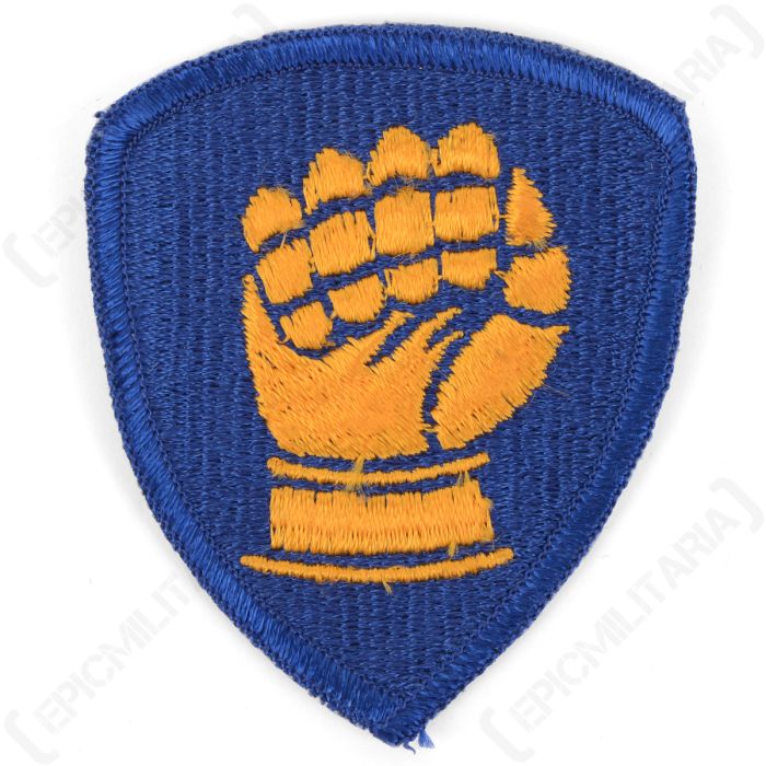 Front of blue, shield-shaped embroidered patch with a gold clenched fist in the middle