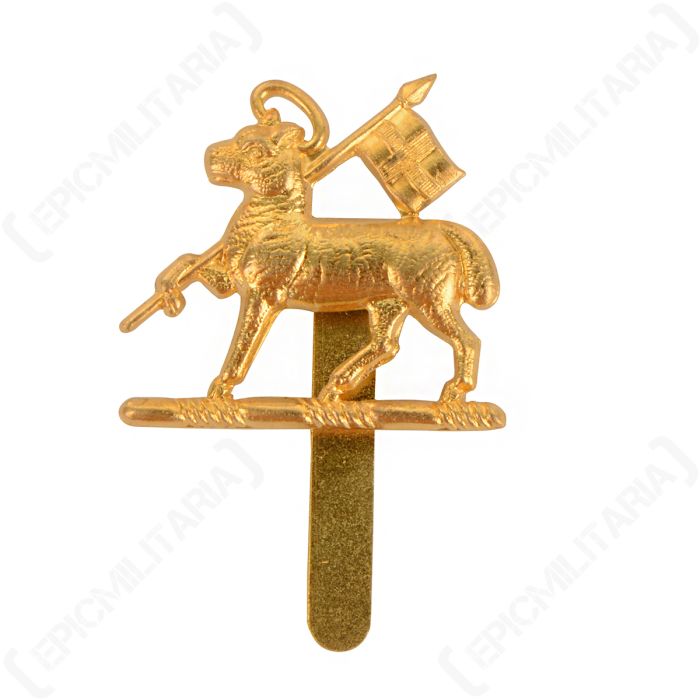 Front of gold coloured British Queens Regiment cap badge featuring a sheep carrying a flag pole