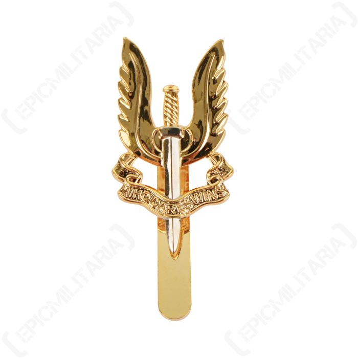 Front of silver and gold coloured British SAS Regiment cap badge showing a verticle sword pointing downward, with a pair of wings behind, and a scroll across the middle with WHO DARES WINS written on it
