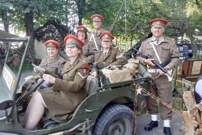 A Jeep with members inside and alongside, wearing British military police uniforms with red cap toppers and weapons