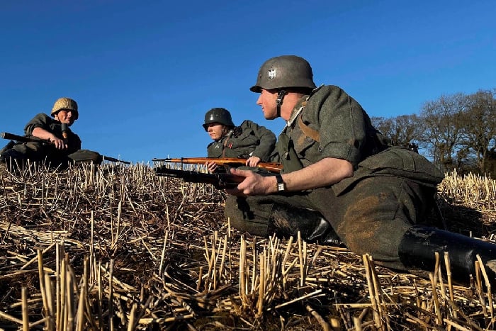 Reenactors in WW2 German uniforms lying in a wheatfield in front of a ridge