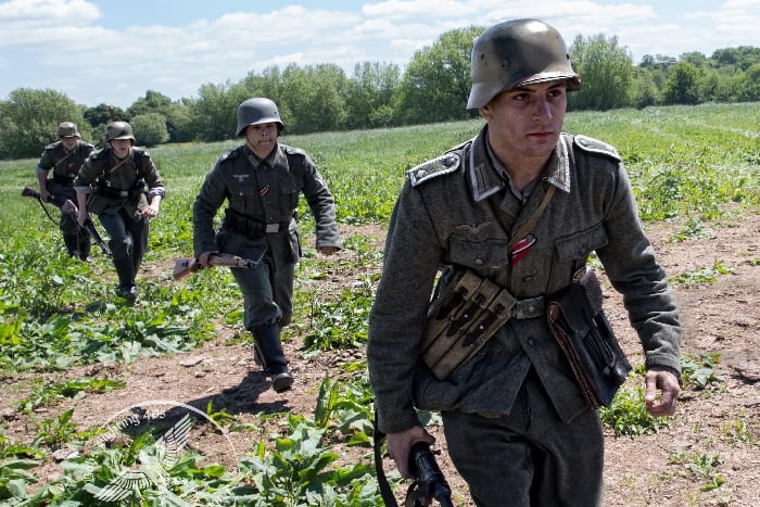 soldiers run towards the camera in a field, dressed in ww2 german uniform