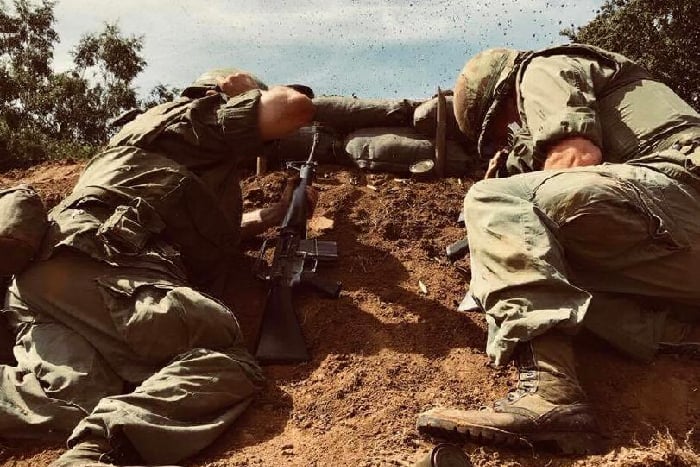 Two vietnam reenactors take cover from an explosion in a foxhole