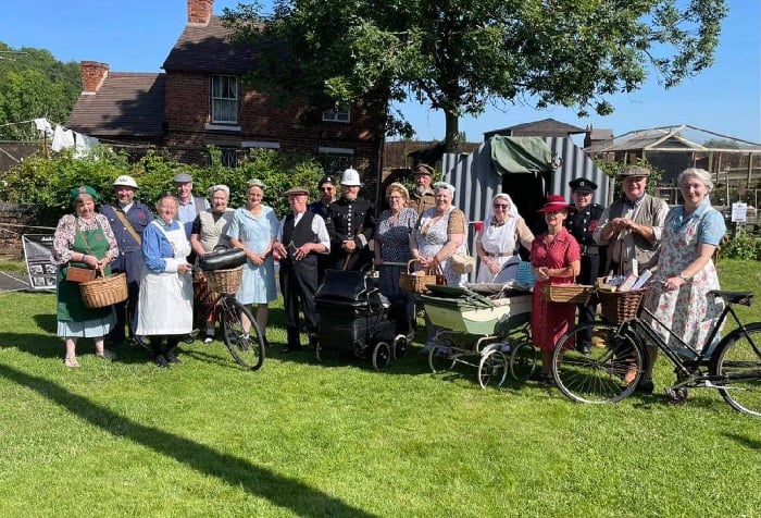 Reenactors dressed as civilians, police, nurses and more pose with bicycles and prams in front of tents and building