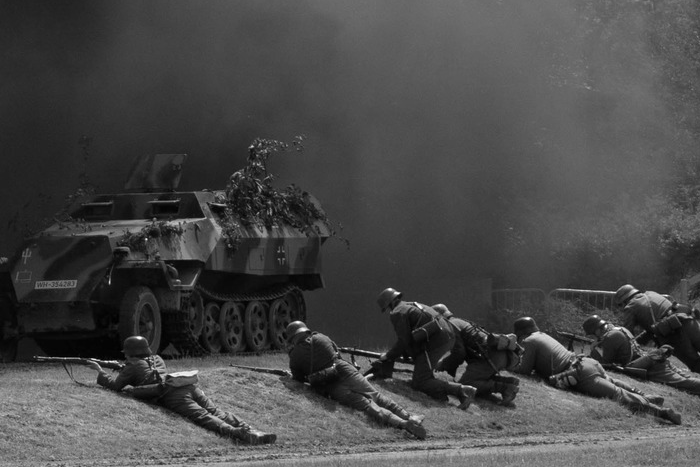 soldiers laying on an embankment with a smoking half-track beyond them