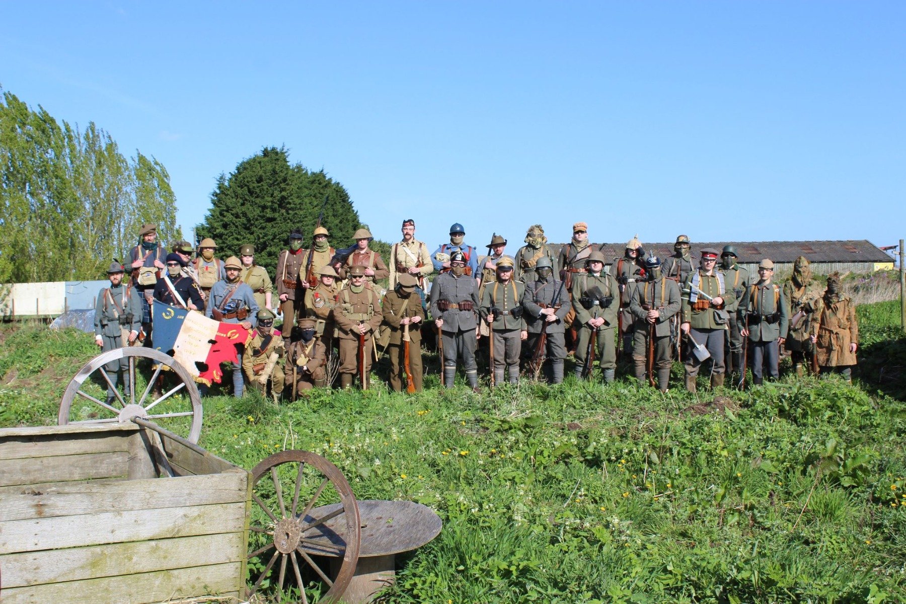 a group of people in World War 1 uniforms of various countries with a French flag standing near a trench with a wooden crate in the foreground.